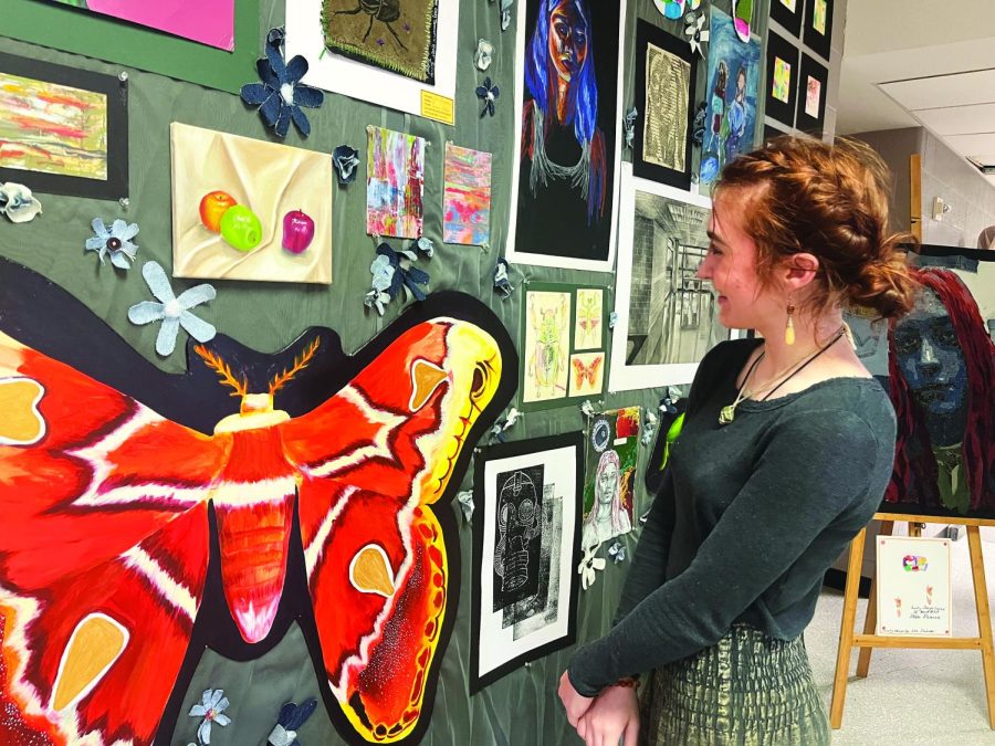 Taking it in…Admiring the different displays at the May 19 Spring Arts Exhibition, Art Studio IV student Julia Dinlocker looks fondly at her work. Dinlocker’s panel featured a large painted moth from her collection of wooden bugs. 
