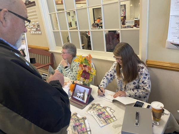 Meeting fans...During an October 18 book signing at Franconia Cafe, “The Lost Cat” author Barbara Brown (right) and illustrator Mia Hershberger sign a copy of their book for local resident Gary Parmer. 