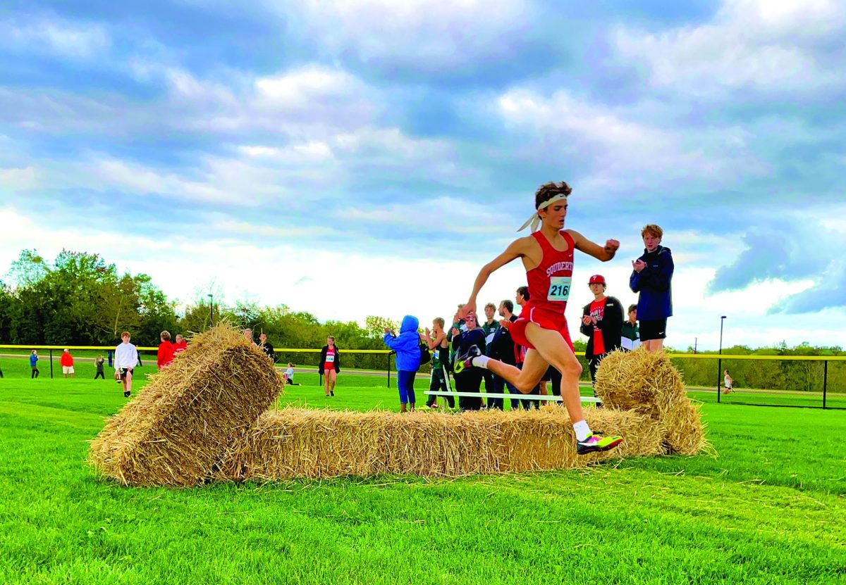 Leaping%E2%80%A6Jumping+over+a+hay+bale%2C+sophomore+Liam+Dougherty+leads+the+pack+at+the+Twilight+Invitational+Meet+on+October+7.+Dougherty+finished+the+race+in+second+place.+