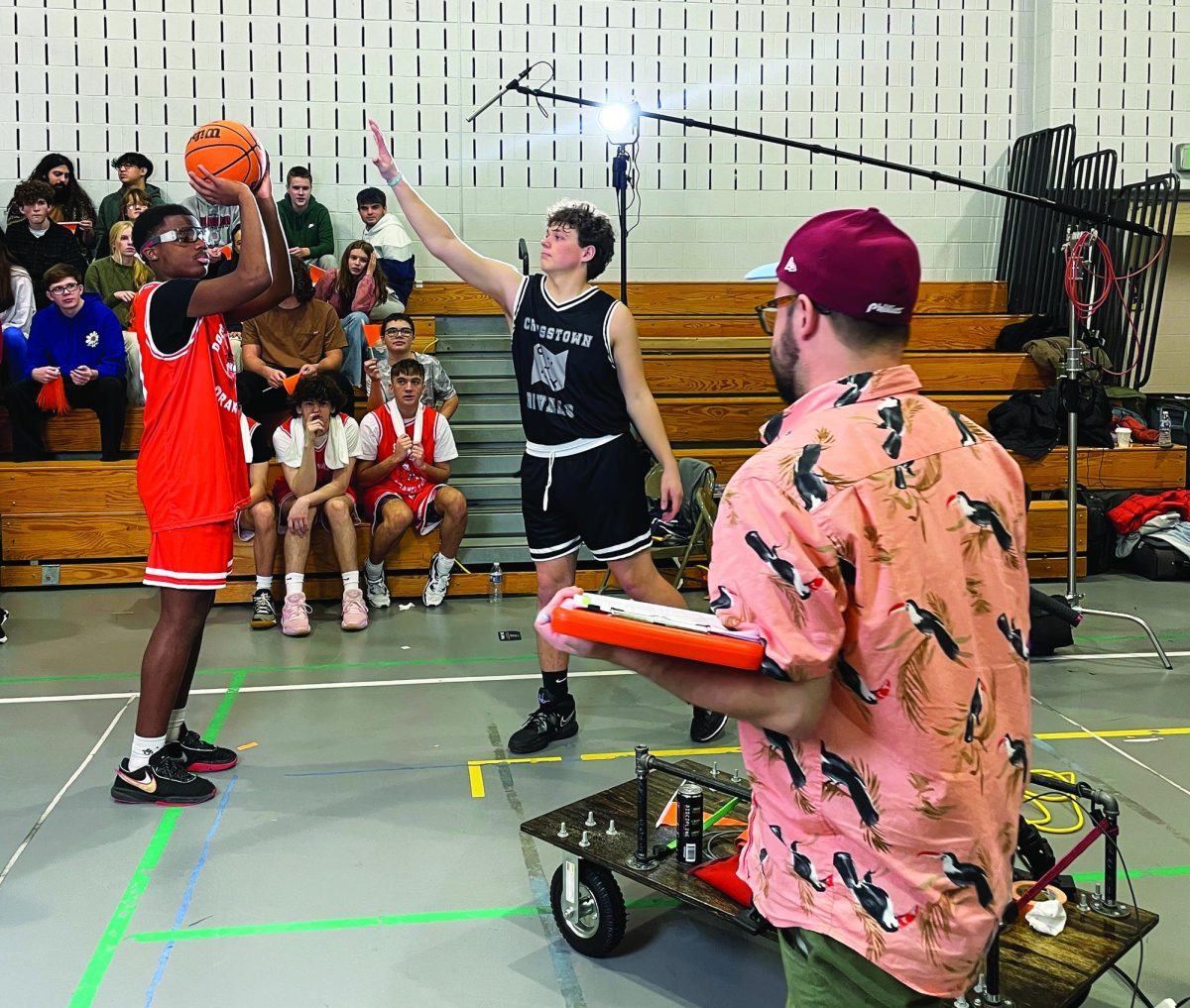Behind the scenes…Acting as basketball players, seniors Zahmere Willis (left) and Griffin Ehret go over the play while graphic designer Kyle Lutz directs. In December, Souderton hosted an Allebach Communications production crew as they filmed commercials for Wise Snacks’ Cheez Doodles brand. 
