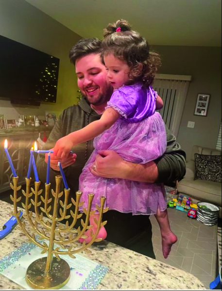 Sparking resilience...Lighting their way through the 2023 holiday season, parent Zach (left) and daughter Ava Margolis light another candle on the Hanukkah menorah. The family enjoyed a day full of fun, gifts and spending time together.