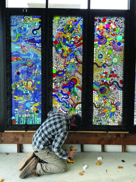 Putting it together...Fixing a bolt, project manager Tim Johnson works on the triptych in the North End Market entryway. The glass panels represent (from left) water, earth and air.